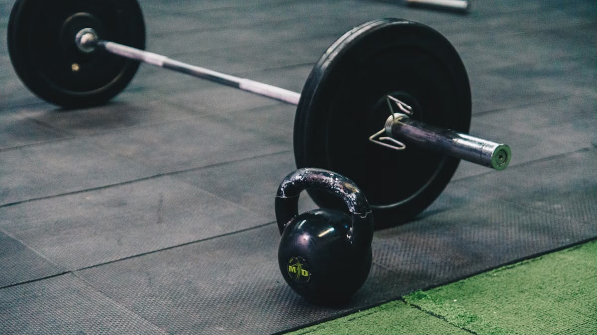 Barbell and kettlebell on gym floor, ideal for fitness and strength training themes.